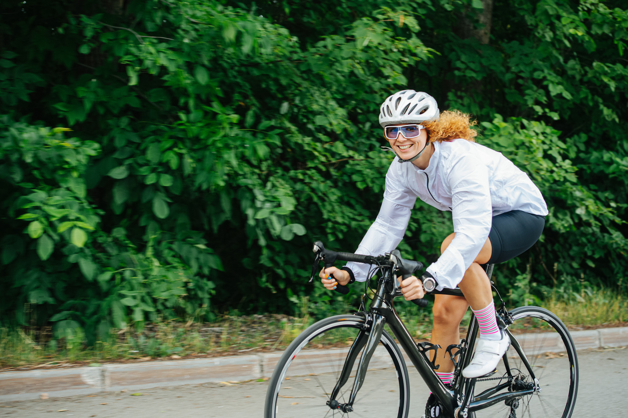 Quirky woman with curly hair in a helmet riding street racing bike on a road