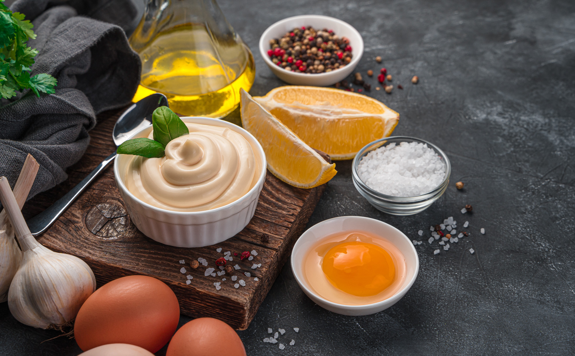Fresh mayonnaise on a dark background with ingredients for its preparation.