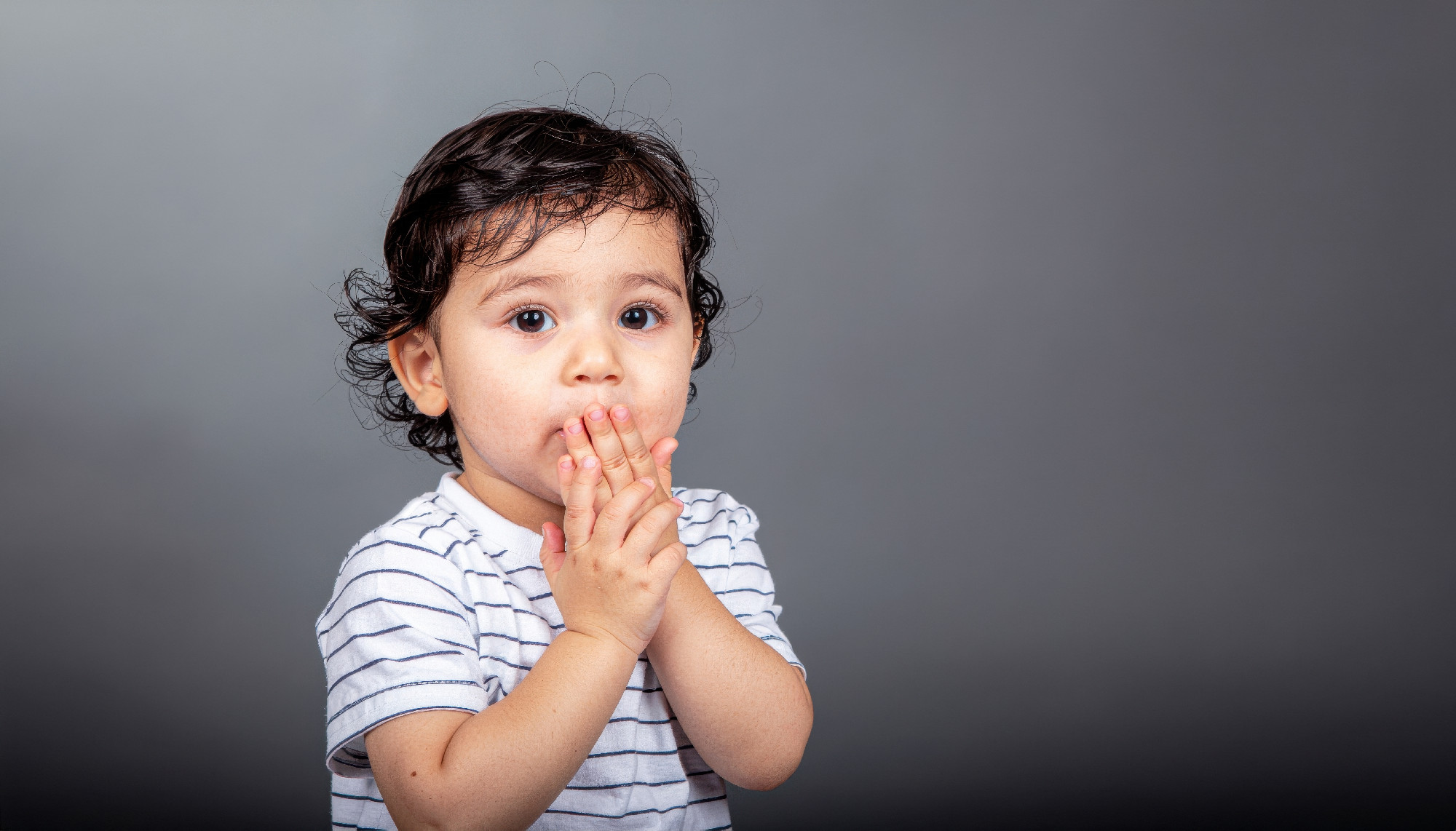 Young child with amused surprise hand to mouth cool gel edge and matte slate background clean studio portrait for education lifestyle and communication
