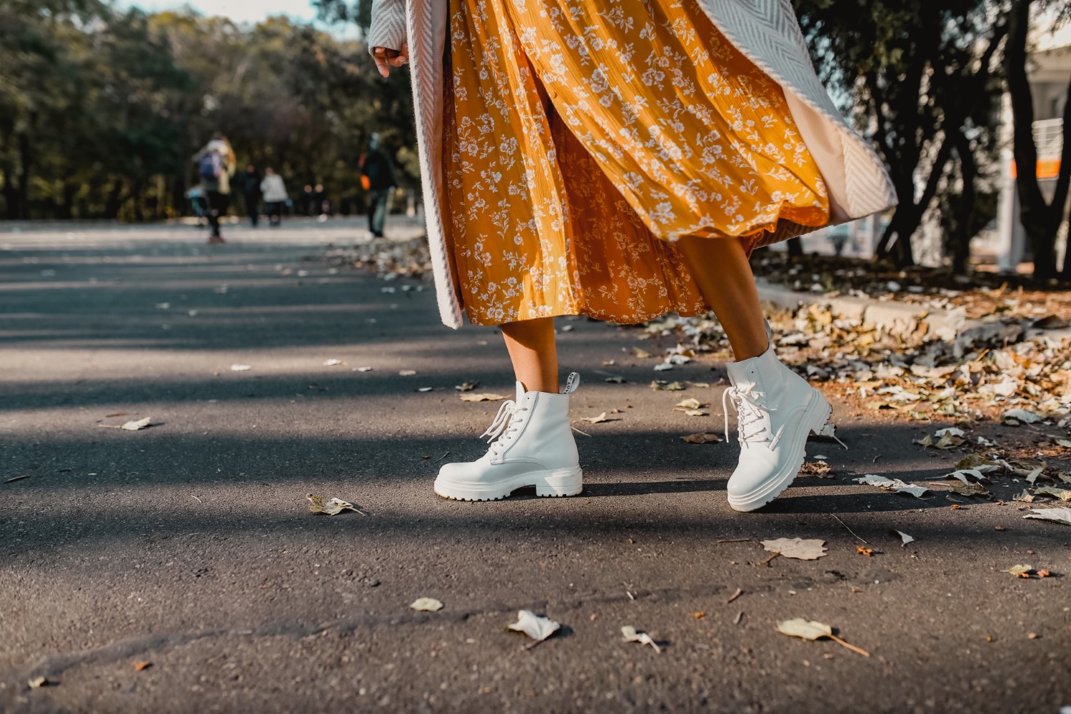 close-up legs in stylish white boots footwear of young woman in yellow printed dress