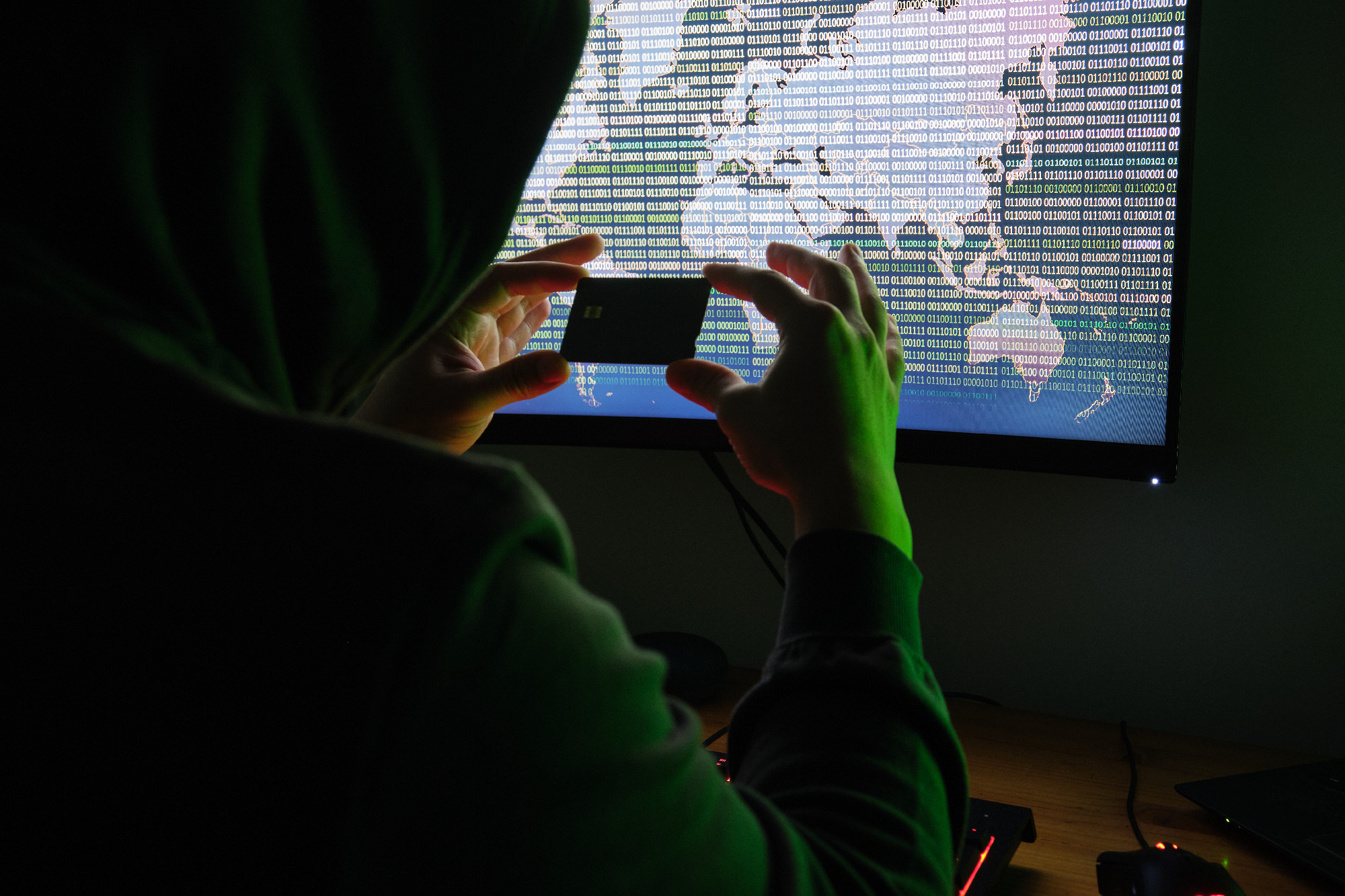 Hacker holding a credit card front of a computer for organizing massive data breach attack around the world. Cyber criminal concept.