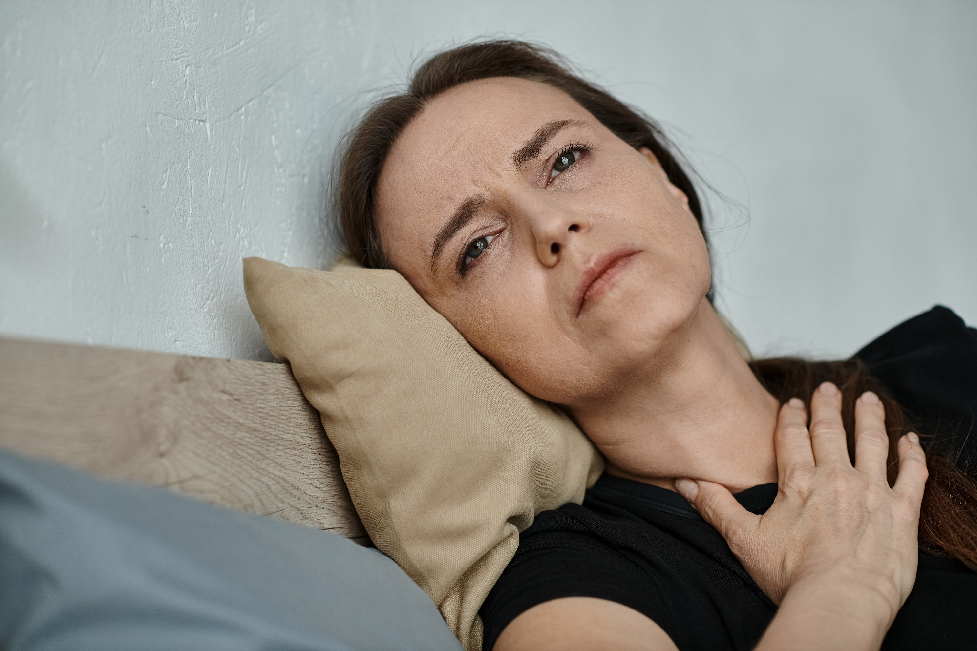 Middle-aged woman lying in bed with hand on chest.