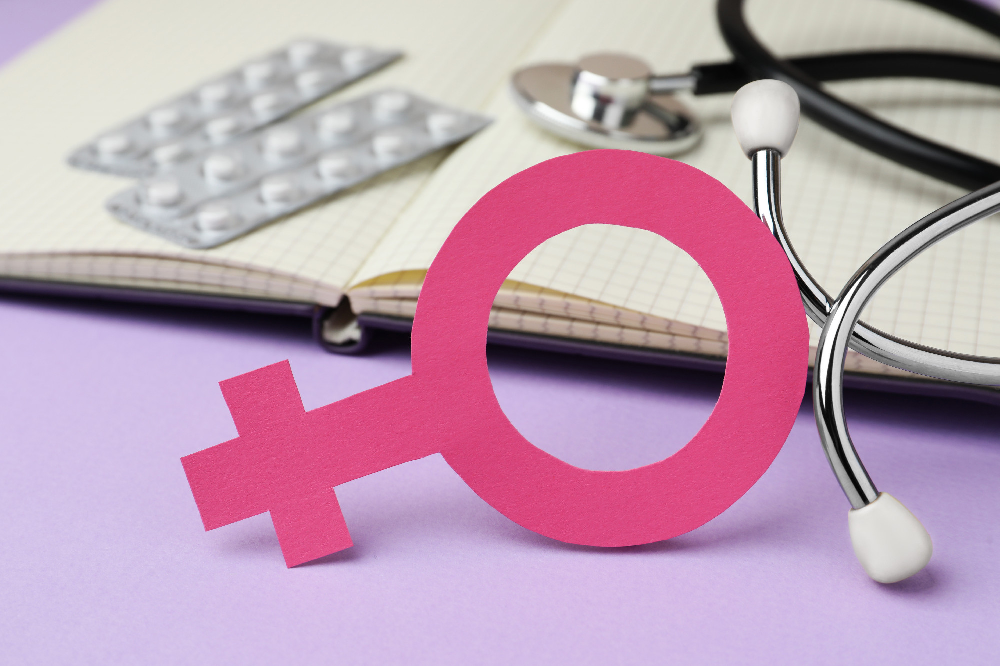 Female gender sign near open notebook, stethoscope and blisters 