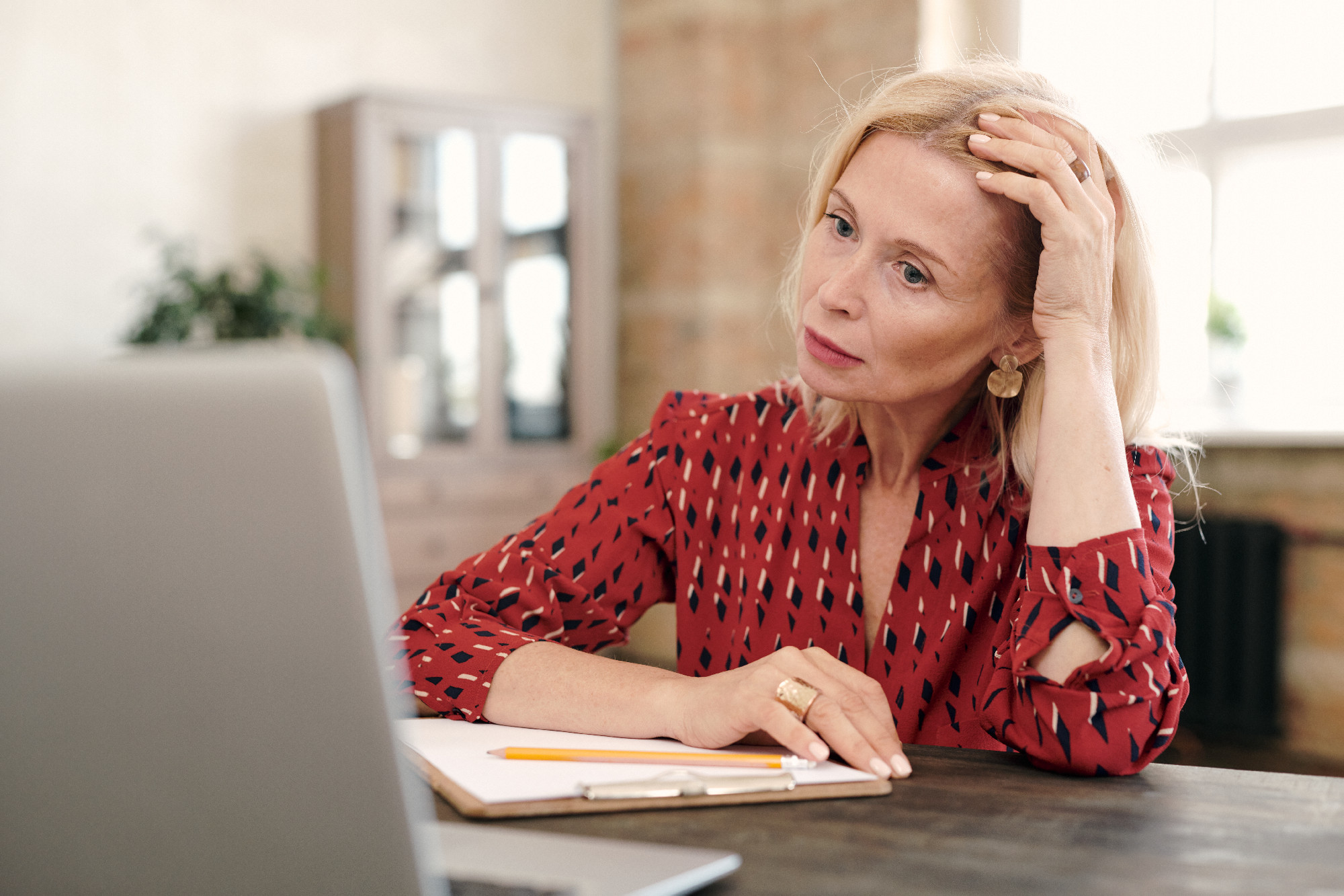 Concentrated mature blond businesswoman sitting in front of laptop by table