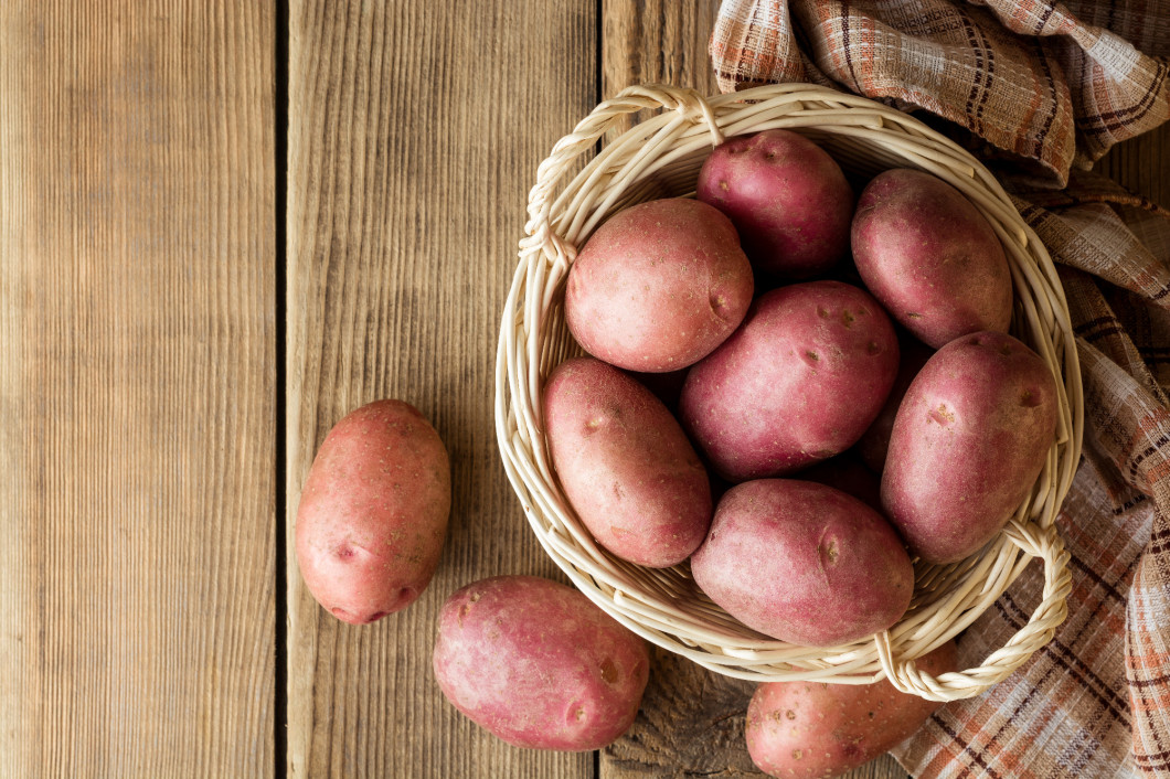 Raw potatoes in basket on wooden background