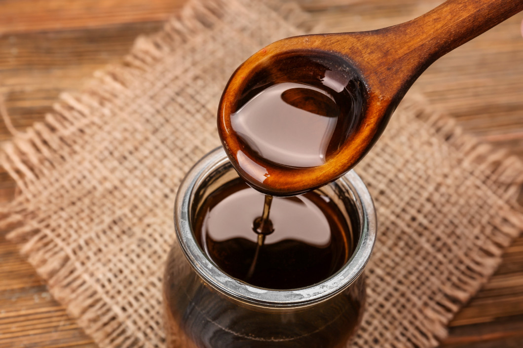 Spoon with tasty caramel sauce over jar, closeup�