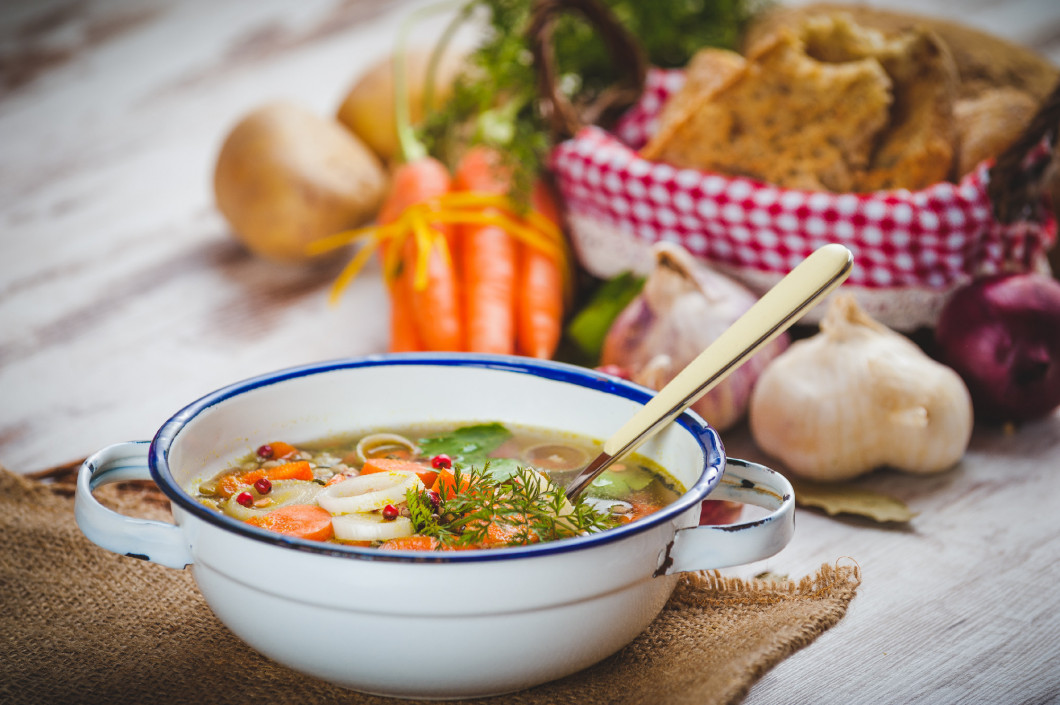 Vegetable soup in a metal bowl on a rural rustic wooden table.