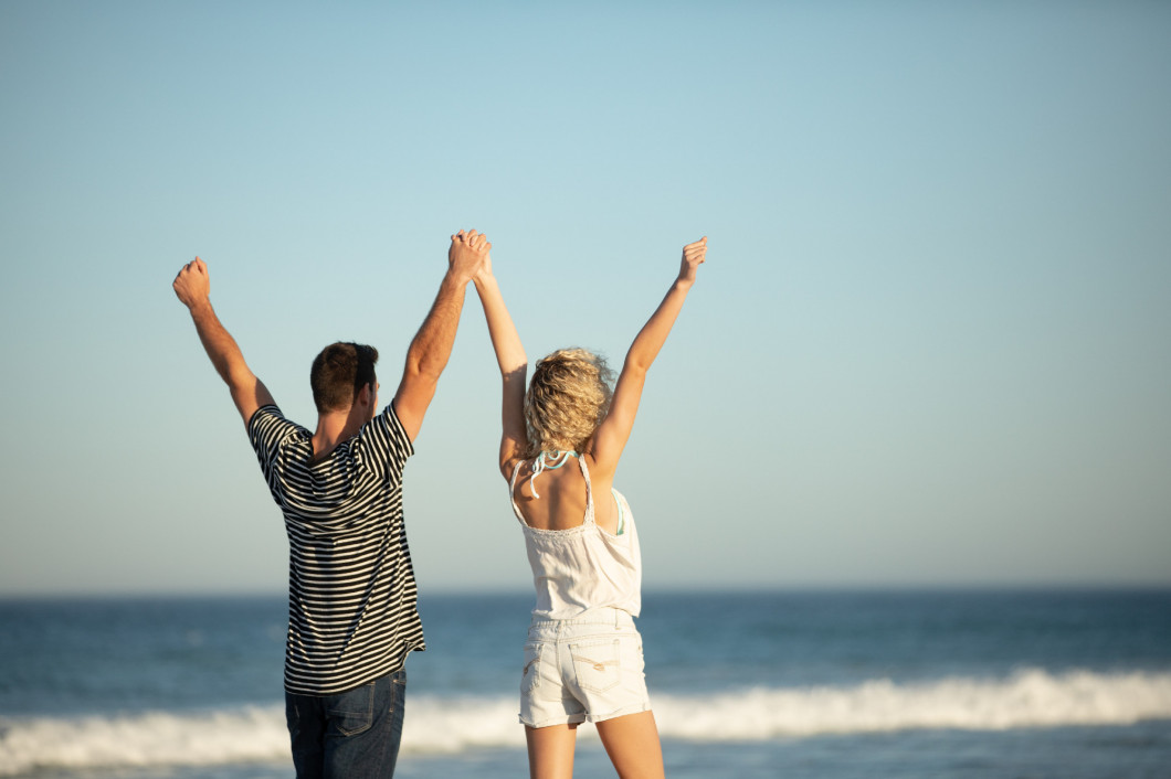 Couple standing together with arms up on the beach