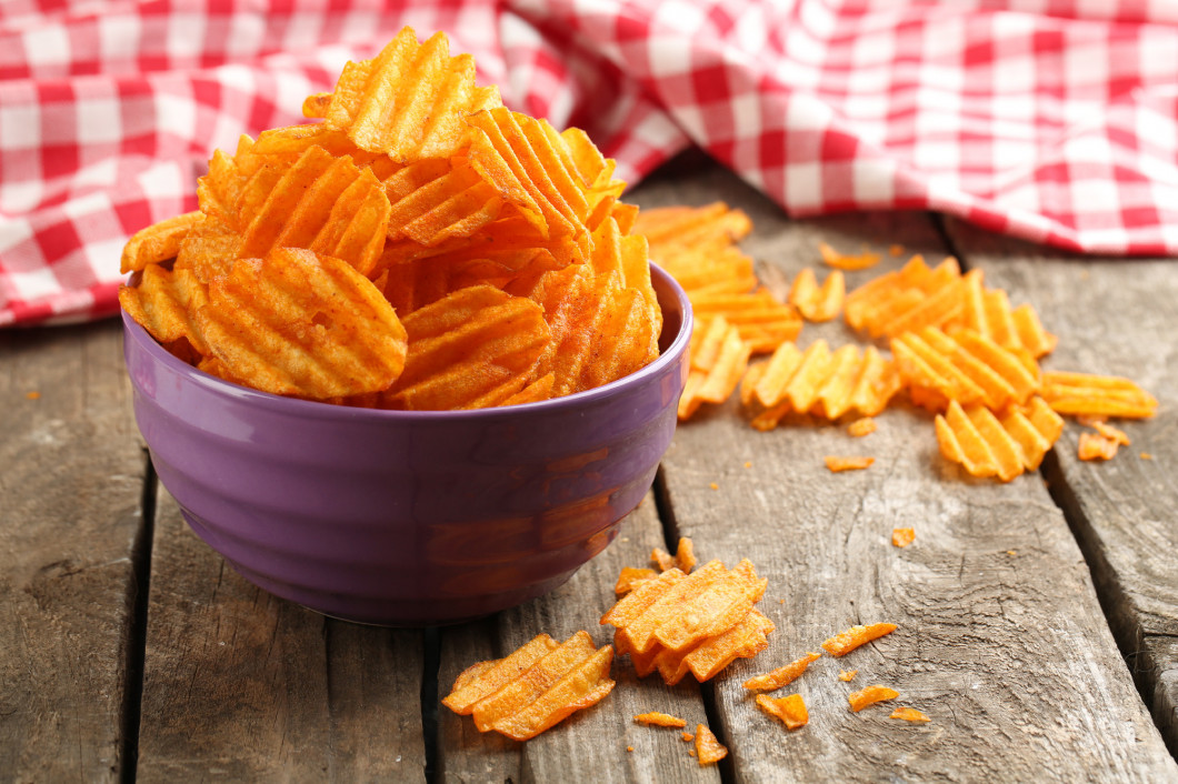 Delicious potato chips in bowl on wooden table close-up