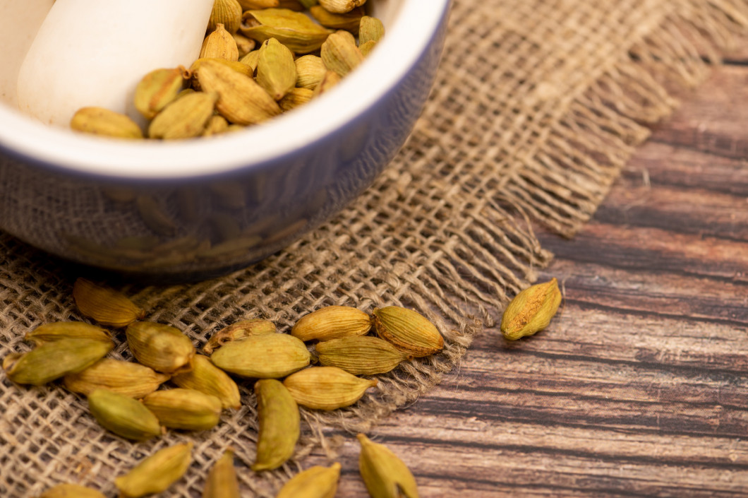 Cardamom in a ceramic mortar and cardamom in a loose background of coarse burlap, close-up, selective focus.