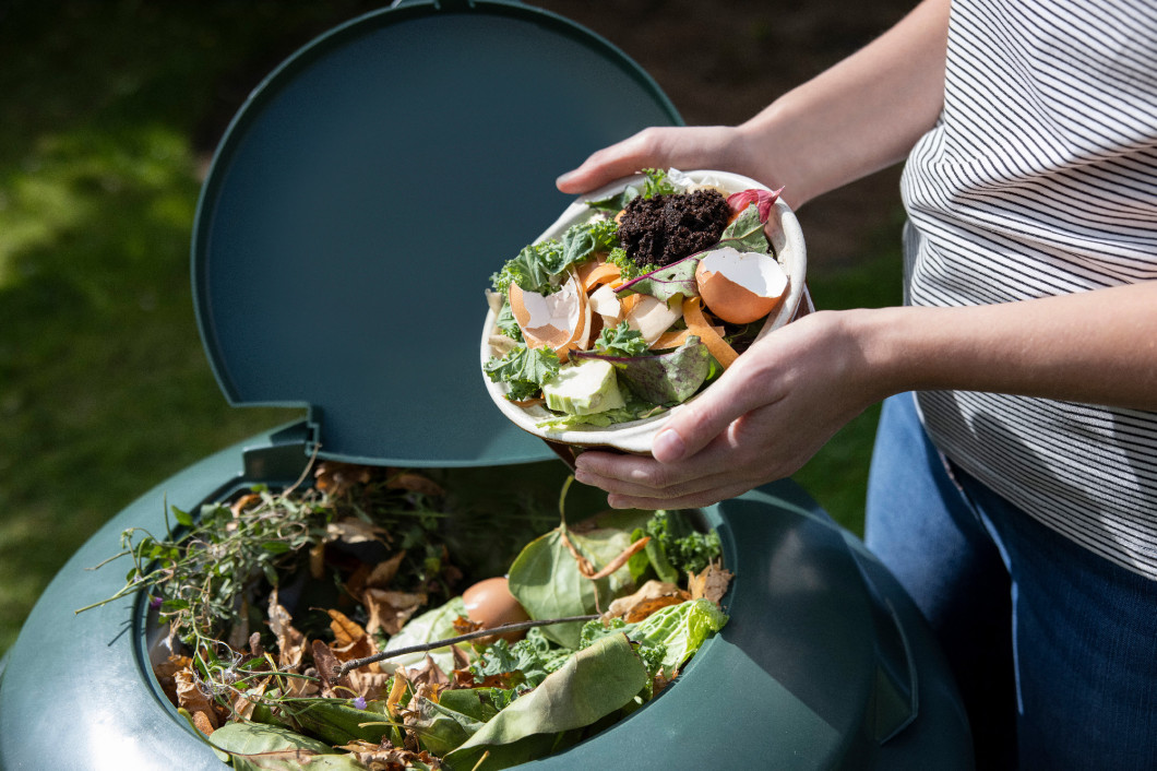 Close Up Of Woman Emptying Food Waste Into Garden Composter At H