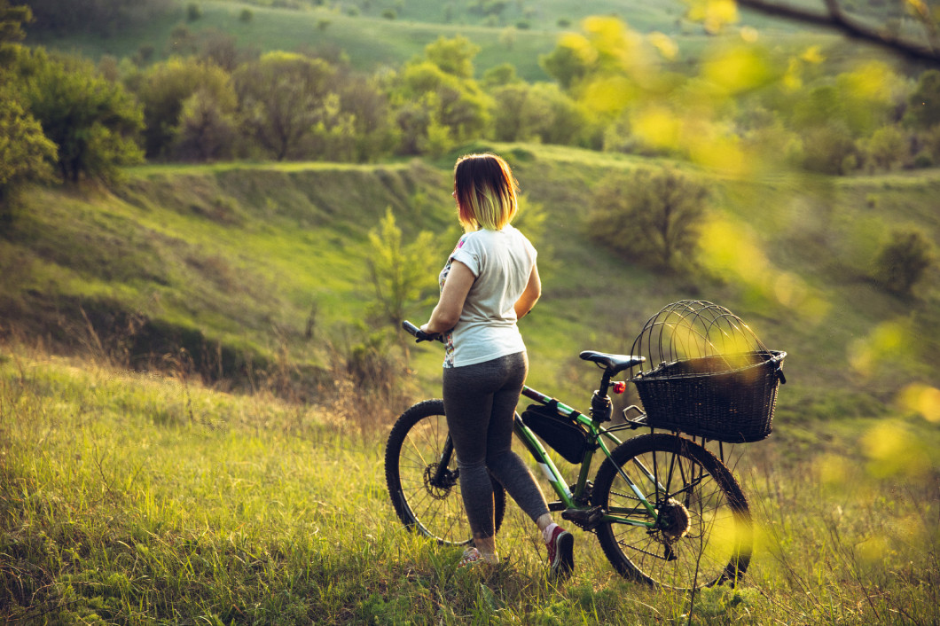 Young woman having fun near countryside park, riding bike, traveling at spring day