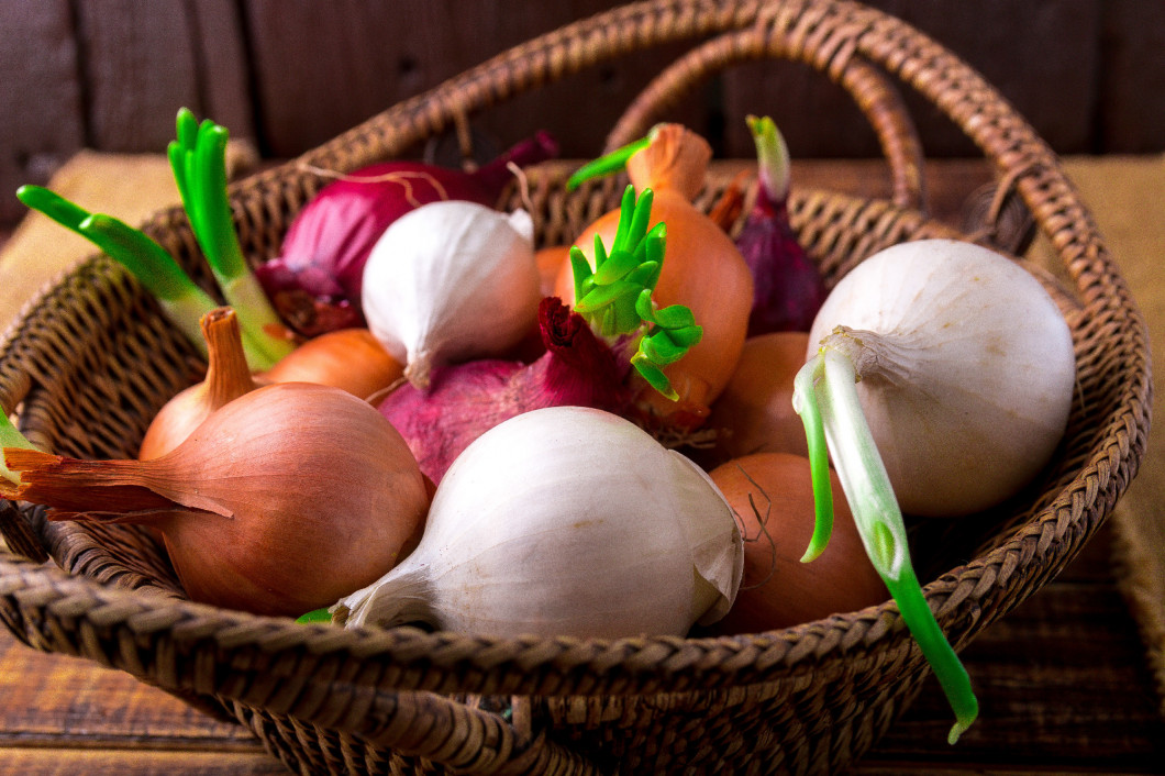 Different onions in basket on wooden background. Rustic style. Copy space. Top view.