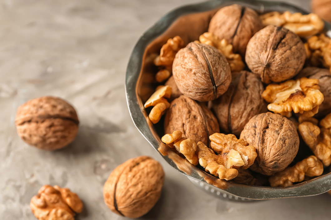 Bowl with tasty walnuts on grey table�