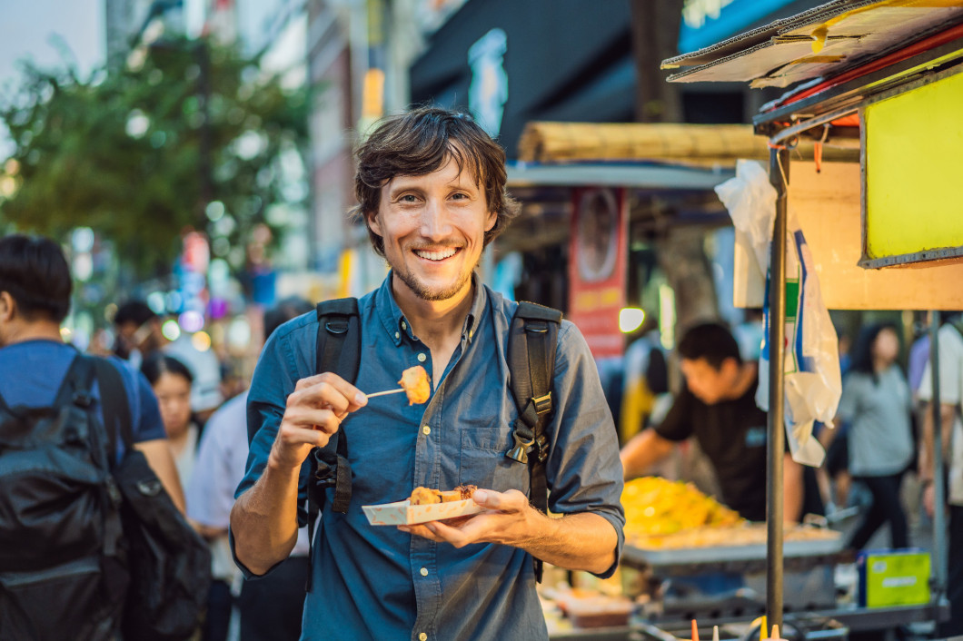 Young man tourist eating Typical Korean street food on a walking street of Seoul. Spicy fast food simply found at local Korean martket, Soul Korea