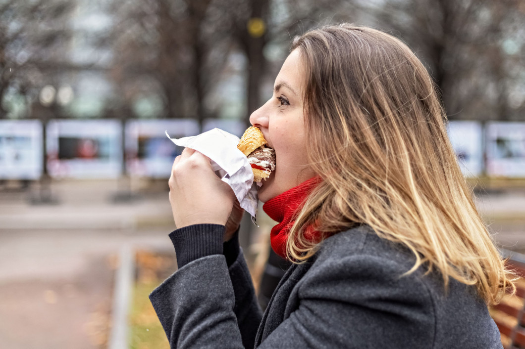 Young hungry woman eats Burger and takes lunch break outdoors in Park.Fast food. Takeaway food concept