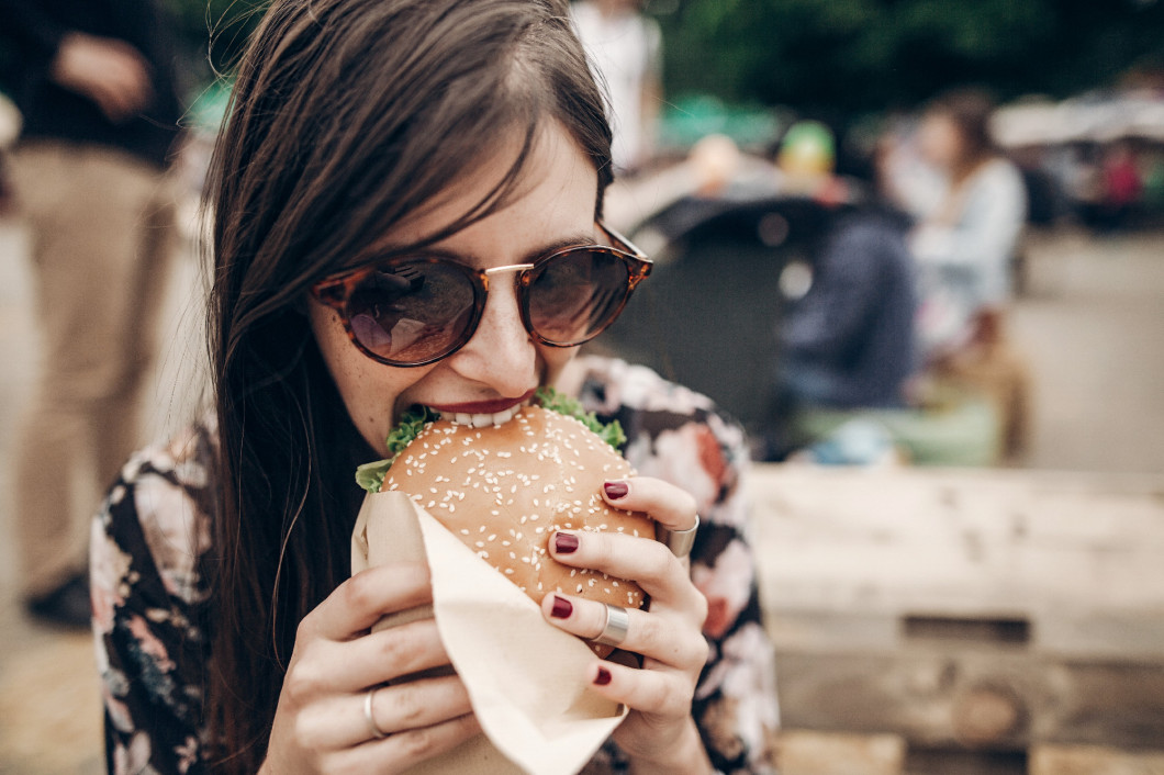 stylish hipster woman holding juicy burger and eating. boho girl