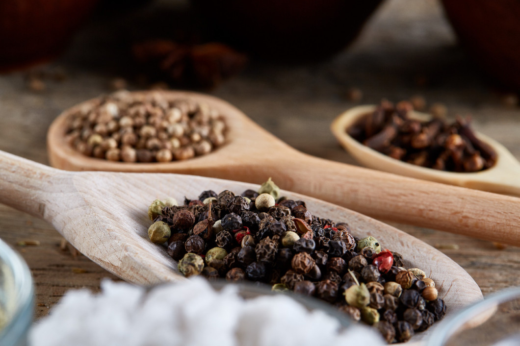 Top view of a wooden spoons full of paprica and black pepper on wooden barrel background, selective focus.