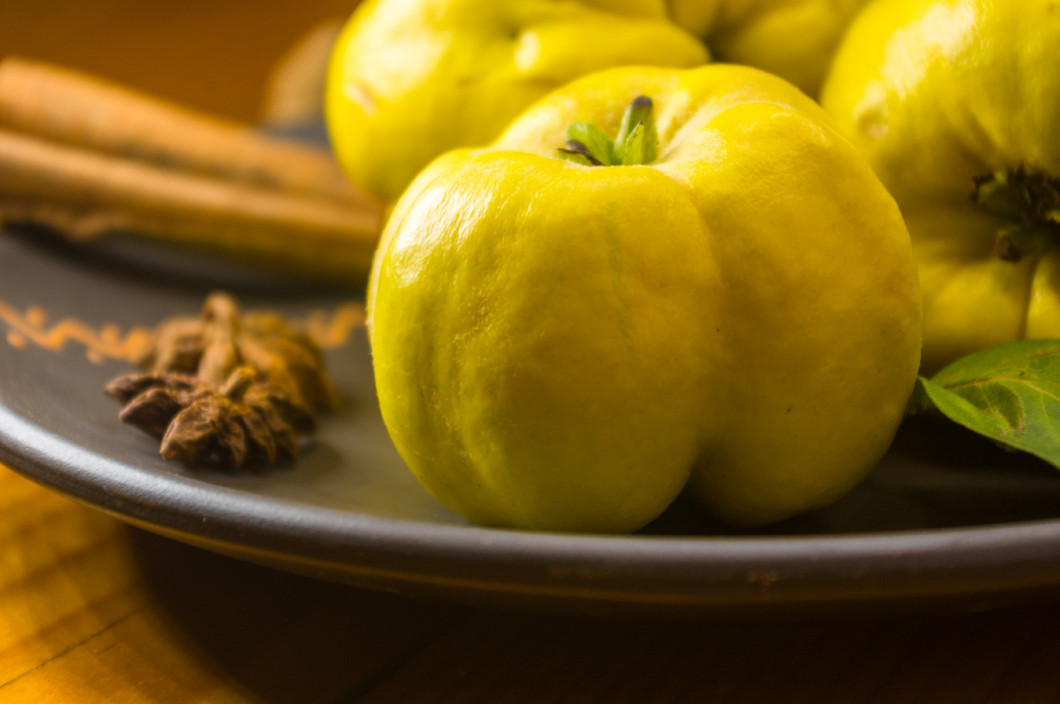 large yellow quince fruits on a ceramic plate, with anise, cinnamon, and walnuts