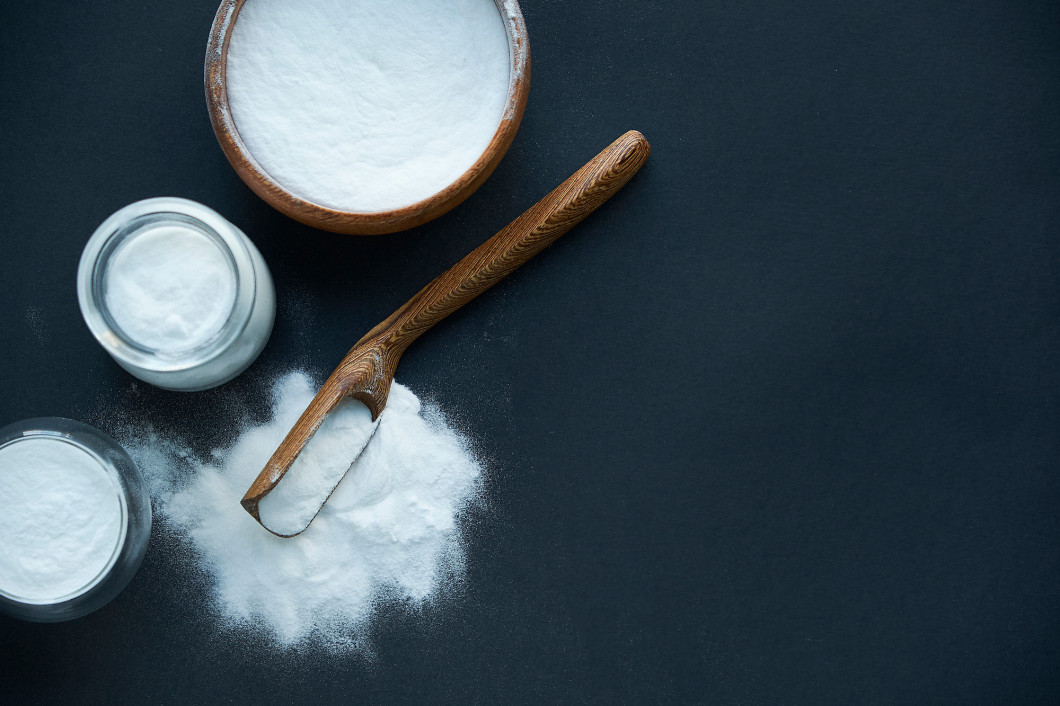 Glass bowl of baking soda. Spoonful of bicarbonate. Top view, flat lay. Close up on a black background. copy space for text.