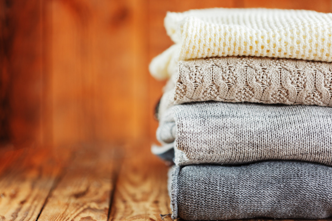 Stack of knitted winter clothes on wooden background, sweaters, space for text