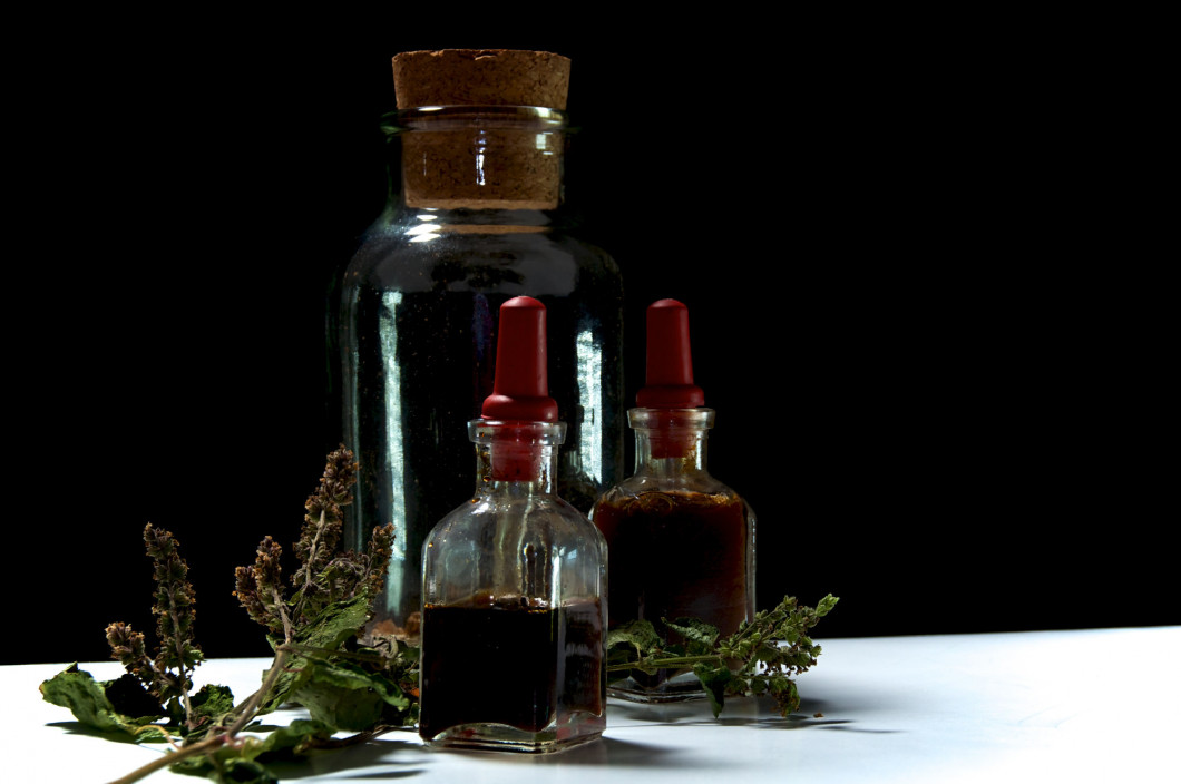 three glass bottles with herbal extracts and dried herbs close t