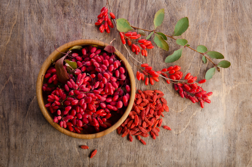 Barberry with leaves and dry goji berries on wooden background