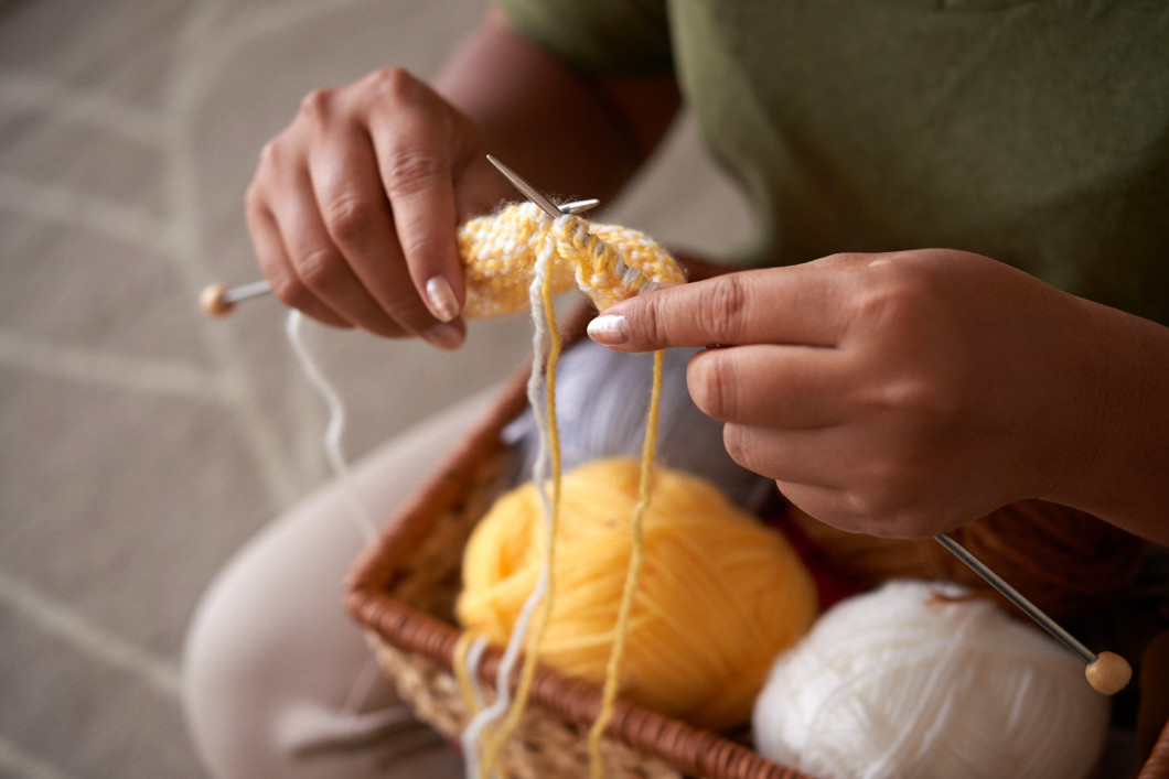 Crop woman knitting on floor