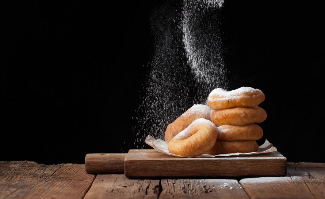 Baker sprinkles sweet donuts with powder sugar on black background. Delicious, but unhealthy food on the old wooden table with copy space