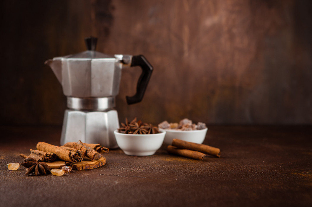 Coffee pot with spices on brown background.