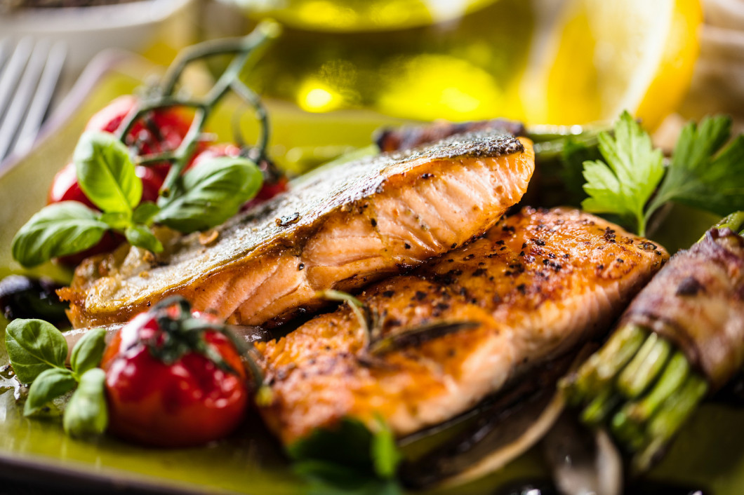 Grilled salmon with vegetables served on green stone plate on wo