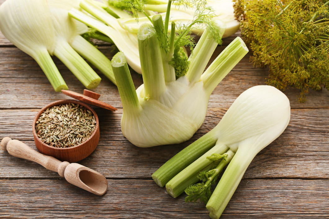 Ripe fennel bulbs and dry seeds in bowl on grey wooden table