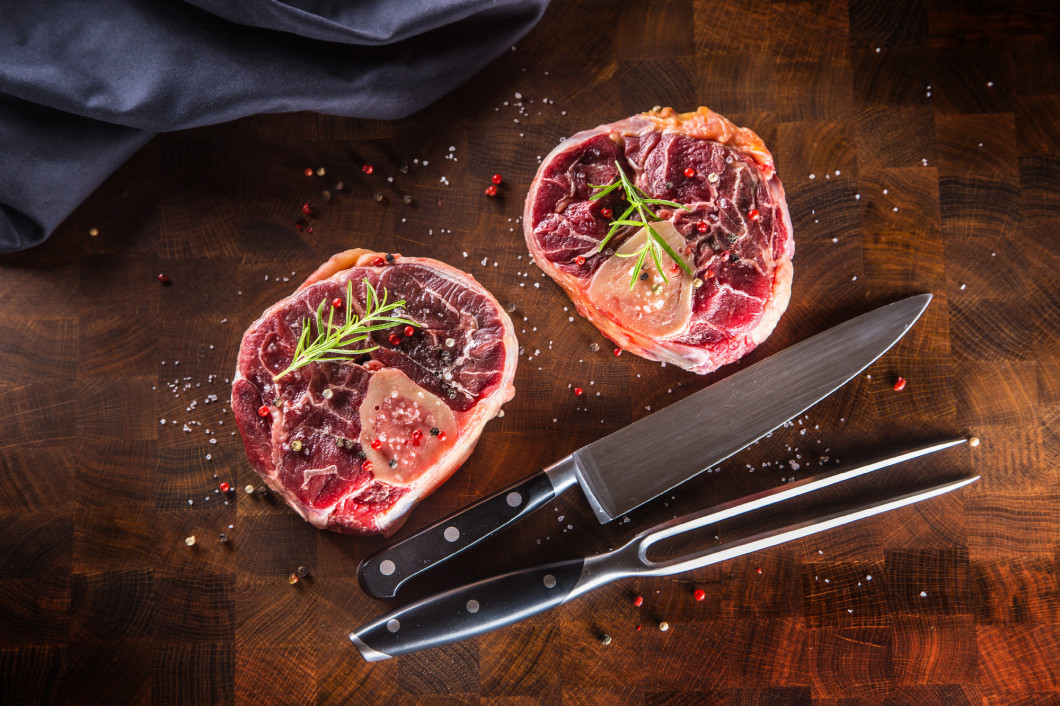 Two raw pieces beef shank on wooden butcher board with fork and 