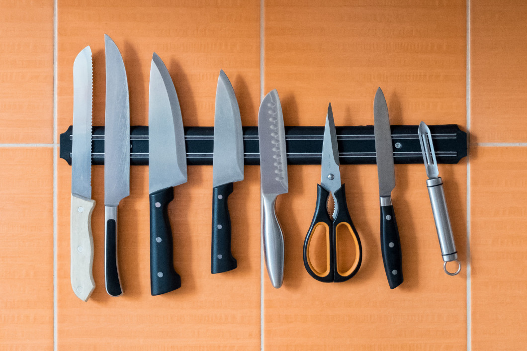 Knives hang on a magnet holder. Orange kitchen wall