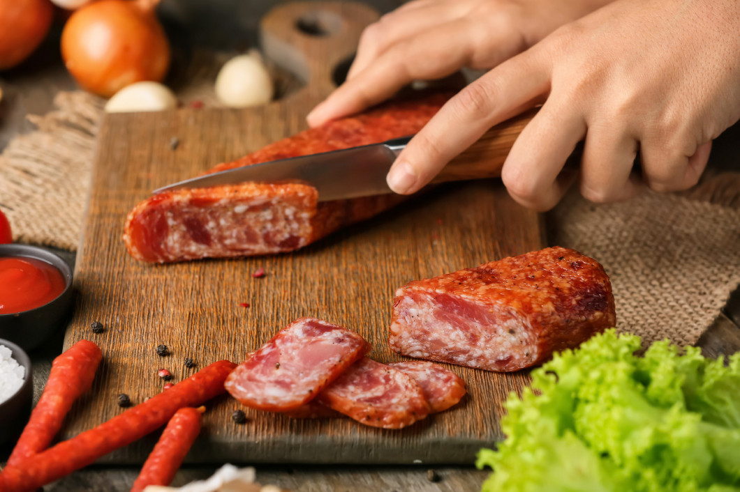 Woman cutting delicious smoked sausage on wooden board�