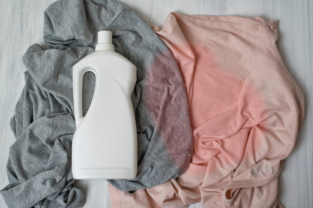 Clothes with stains and a bottle of detergent. Top view