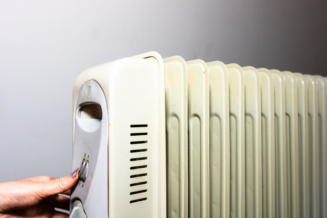 Hands turning on the oil radiator heater on white background