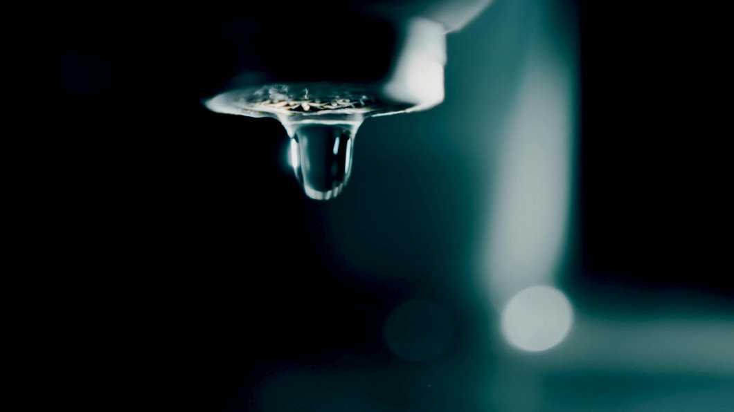 Slow motion shot of water drops falling from the faucet in dark 