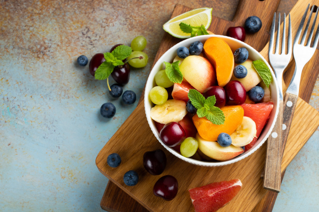 Bowl of healthy fresh fruit salad on a blue rusty background. Top view with copy space. Flat lay