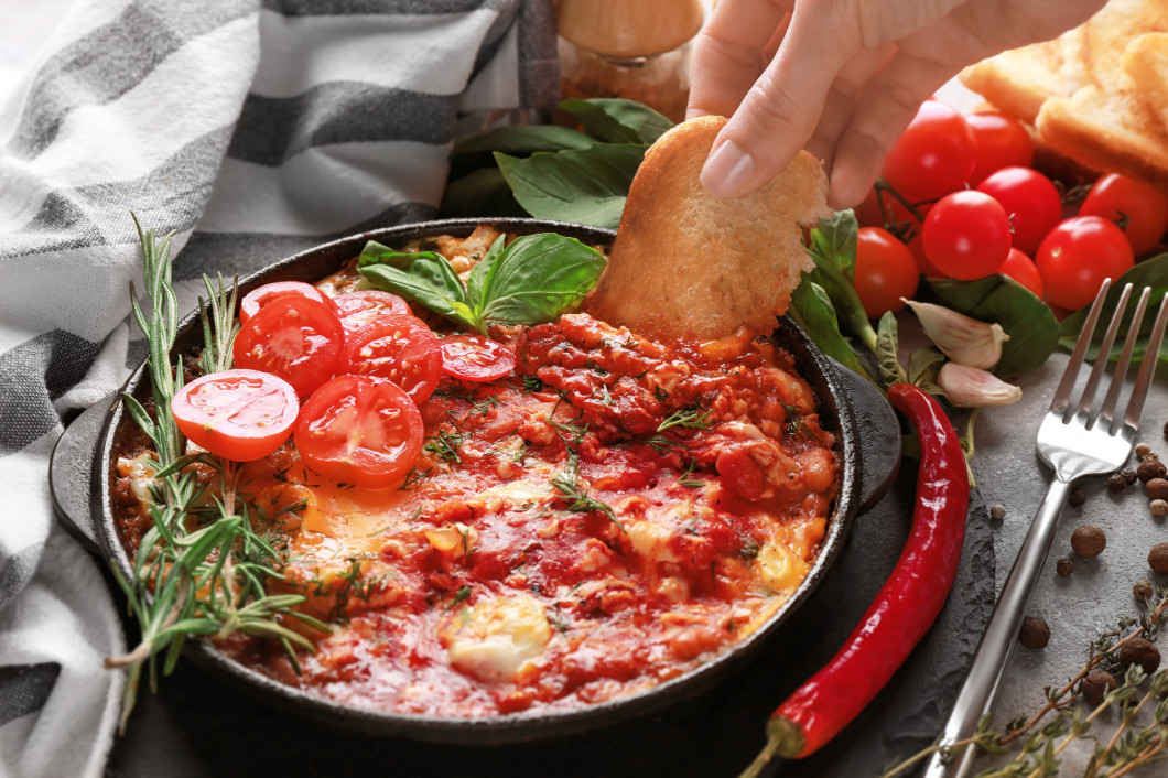 Woman dipping bread into eggs in purgatory on table�