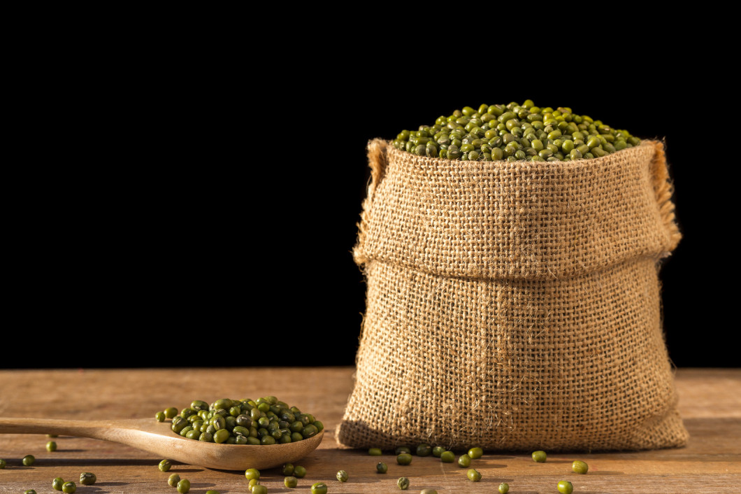 Mung beans in small wooden sack on wooden table. Isolated on bla