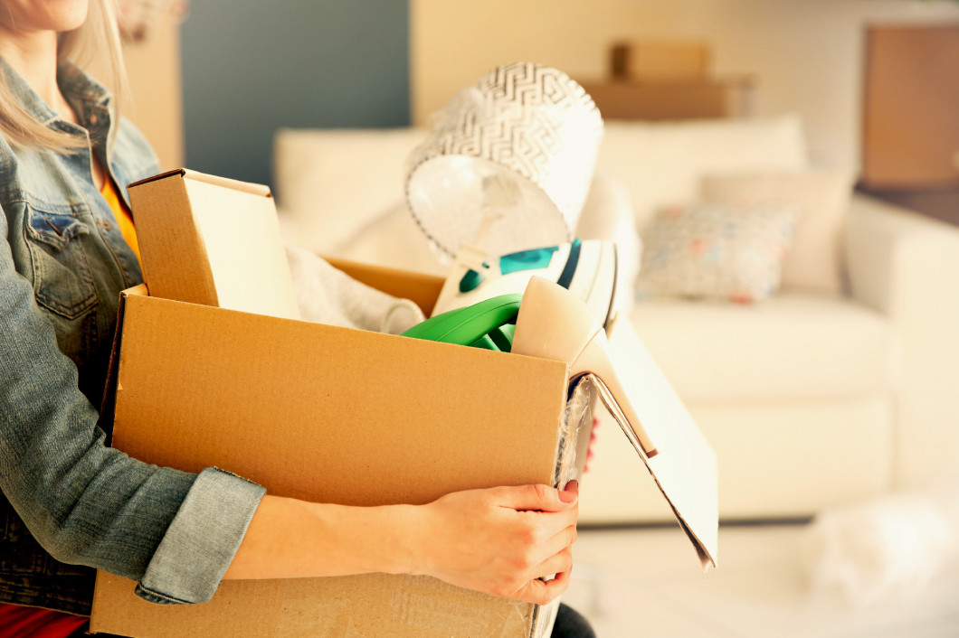 Young woman holding open cardboard box with things for moving in