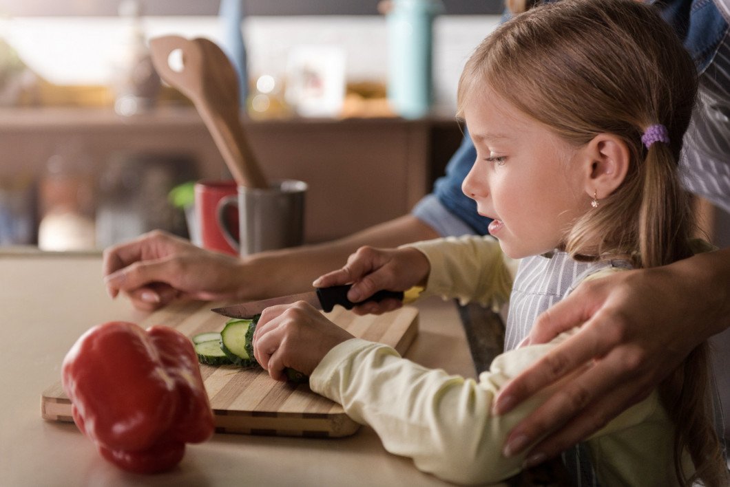 Concentrated little girl cutting a cucumber with her mother