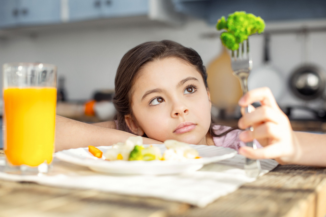 Serious child looking at the vegetable on her fork