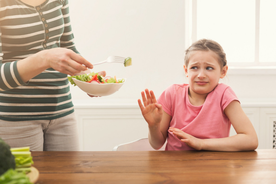 Woman offering her daughter salad but girl refusing