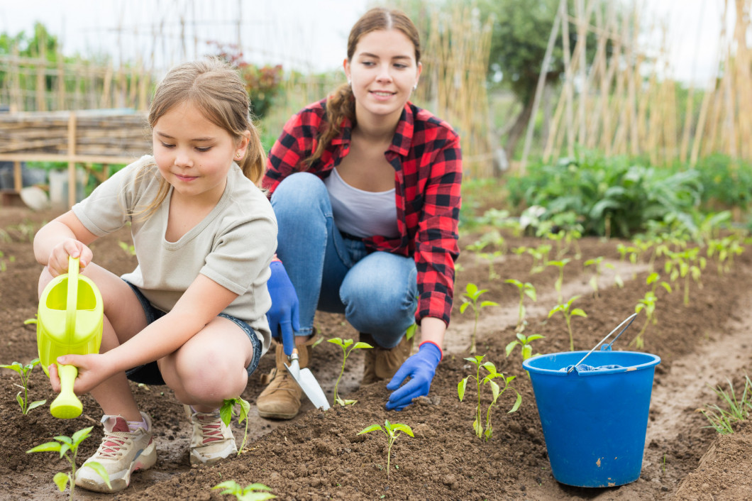 Woman with little girl watering plants in garden closeup