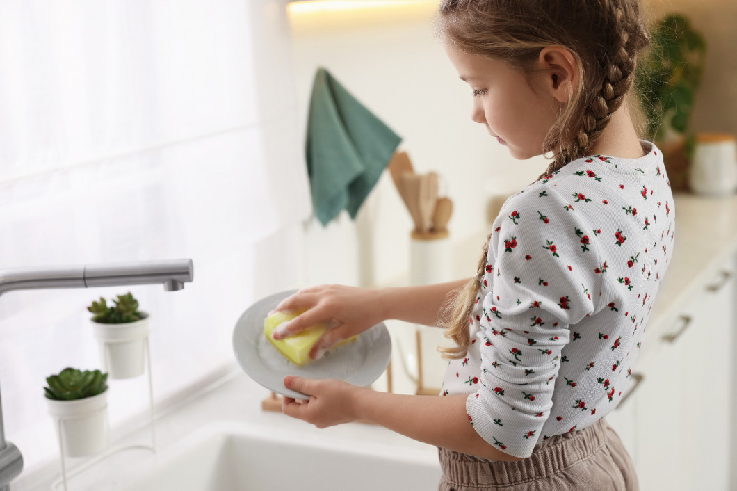 Little girl washing plate above sink in kitchen