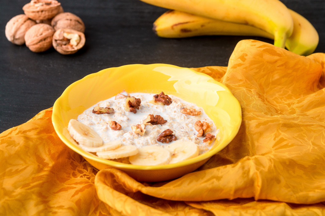 Oatmeal with walnuts and banana in yellow bowl on black background.. Healthy breakfast.