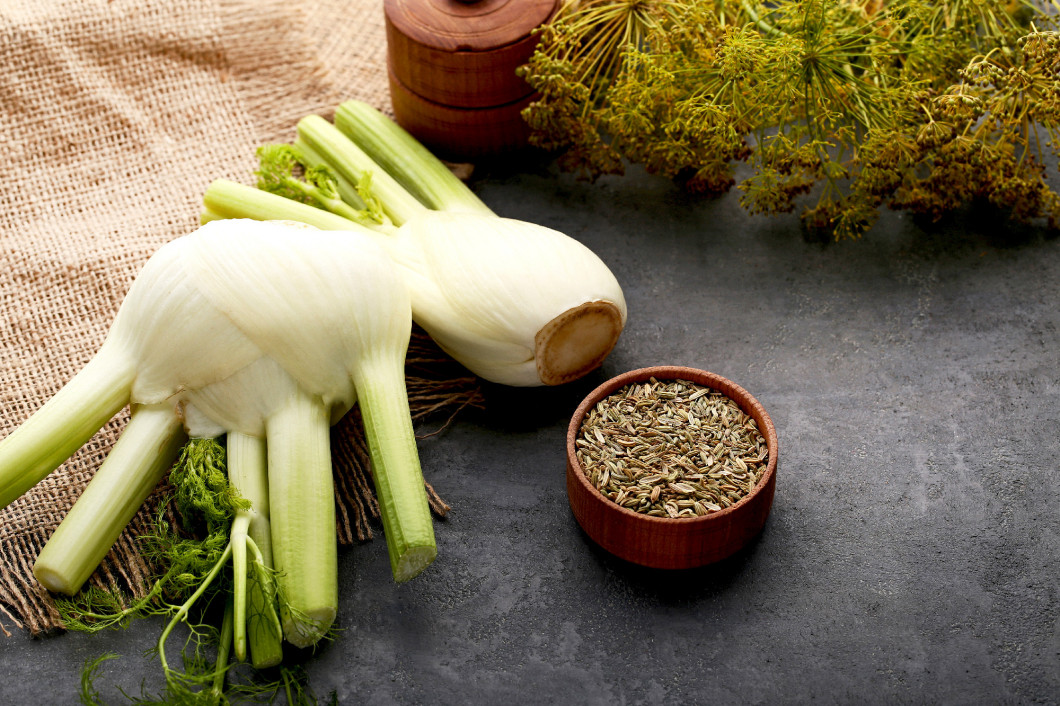 Ripe fennel bulbs and dry seeds in bowl on grey wooden table