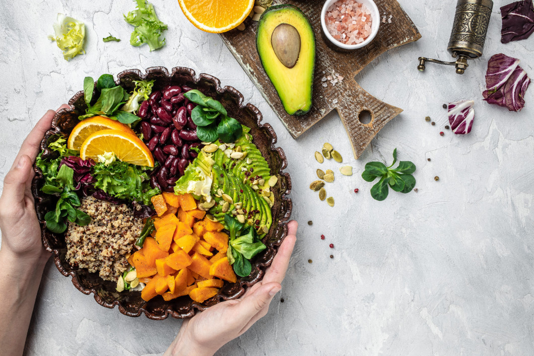 Female hands holding Quinoa salad in bowl with avocado, sweet potato, beans on light background. superfood concept. Healthy, clean eating concept. Vegan or gluten free diet. top view